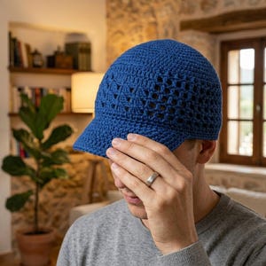 Könnte beinhalten: Eine leuchtend blaue Häkel-Baseballkappe mit einem strukturierten, offenmaschigen Muster an der Krone und einem festen Schirm. Die Mütze ist aus Garn mit sichtbaren Maschendetails gefertigt und bietet eine strukturierte und flexible Passform.