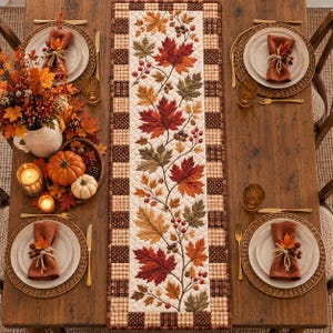 May include: A rectangular quilted table runner featuring a central panel with a printed pattern of autumn maple leaves, berries, and acorns, bordered by a brown and tan checkered fabric frame, displayed on a wooden dining table with place settings.