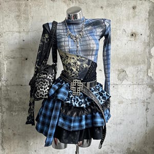 Completo coordinato 2 pezzi Y2K Punk Alt con top a quadri blu leopardati, collo alto in rete trasparente, maniche lunghe e minigonna a balze in pelliccia sintetica.