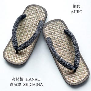 May include: A pair of zori sandals featuring a woven straw footbed with a dark brown border. The fabric thong straps, known as hanao, are black with a white seigaiha wave pattern. Text on the image reads Ajiro, Hanao, and Seigaiha.