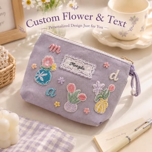 Puede incluir: Un estuche con cremallera de color lavanda que presenta parches bordados de jarrones con flores, pequeños detalles florales y un parche rectangular blanco con borde de encaje con el nombre Mengda bordado en negro. Incluye las letras minúsculas m, a y d.