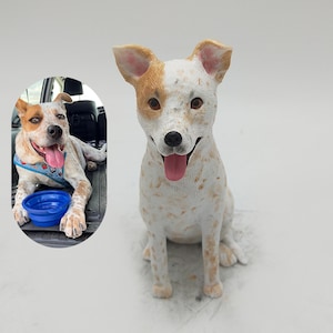 May include: A hand-painted dog figurine featuring a white coat with tan spots and patches, pointed ears, and an open mouth with a pink tongue. Beside it, a circular inset shows a real dog with similar markings wearing a blue harness and collar.