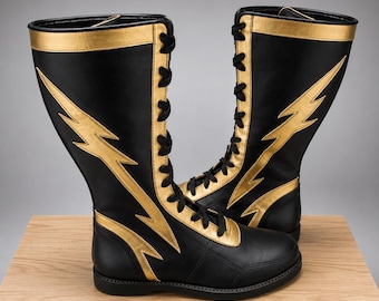 May include: A pair of knee-high black boots featuring gold lightning bolt accents on the sides, gold trim along the top and lace panels, and black laces. The boots have a rounded toe and a flat sole, with a structured design and a smooth finish.
