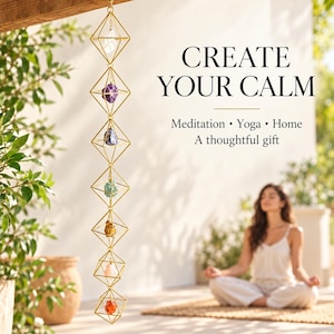 May include: A vertical hanging mobile featuring seven gold-toned geometric wire frames, each containing a different colored raw crystal. The text reads: CREATE YOUR CALM, Meditation • Yoga • Home, A thoughtful gift.