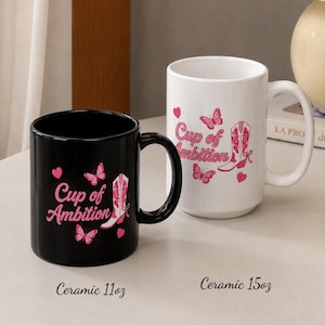 May include: A black ceramic 11oz mug and a white ceramic 15oz mug, both featuring the pink text Cup of Ambition, pink butterfly illustrations, and a pink cowboy boot graphic. The mugs are displayed side by side on a flat surface.