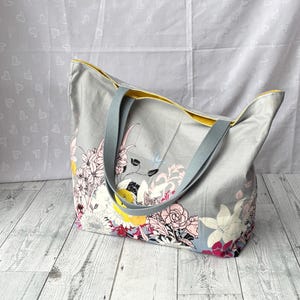 May include: A gray tote bag with yellow trim and floral print. The bag has two long straps.