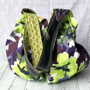 May include: A large, floral print tote bag with a black and green strap. The bag is made of fabric and has a loose, slouchy shape.