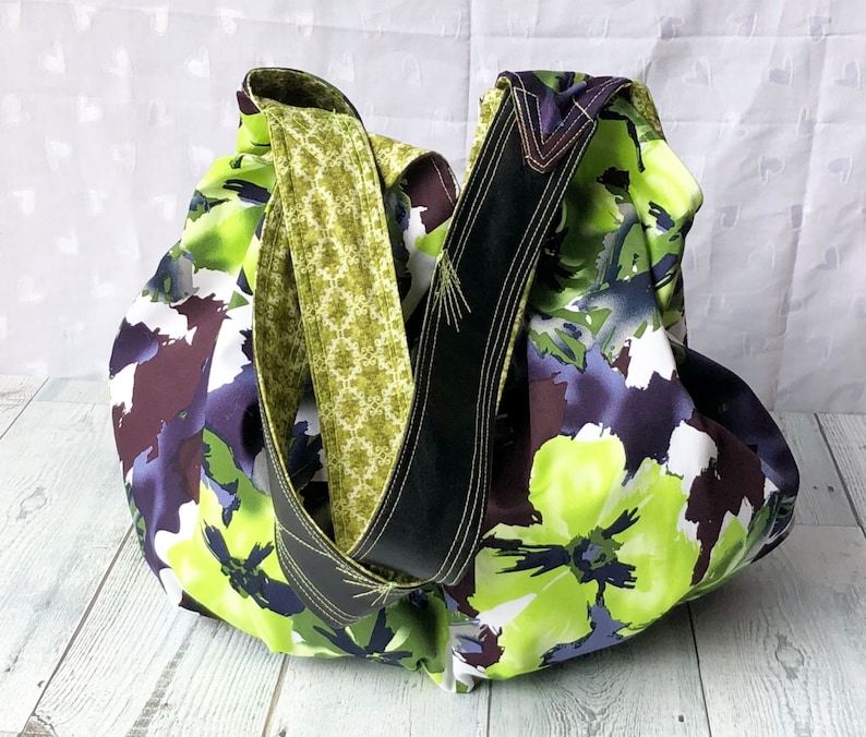 May include: A large, floral print tote bag with a black and green strap. The bag is made of fabric and has a loose, slouchy shape.