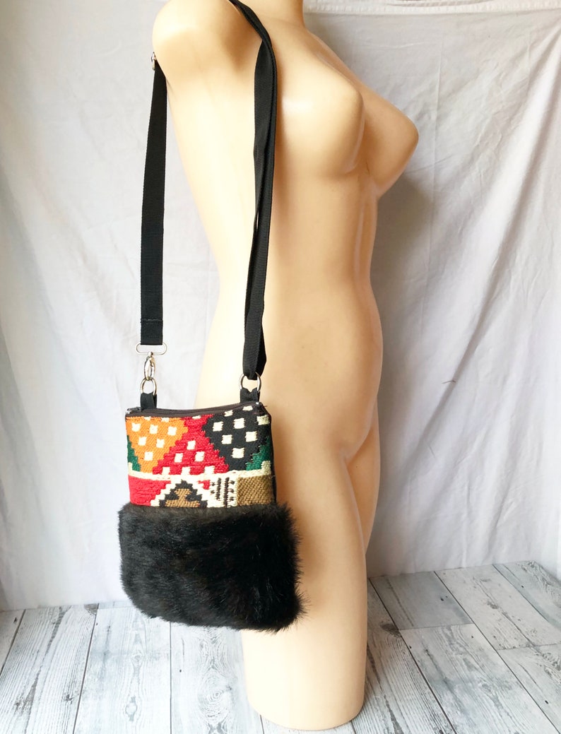 Pu&ograve; includere: Una piccola borsa a tracolla colorata con motivo geometrico e bordatura in pelliccia sintetica nera. La borsa ha una tracolla nera regolabile.
