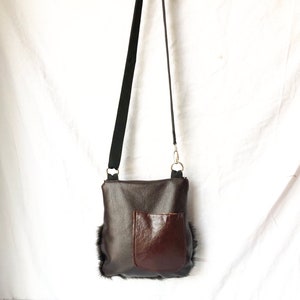Pu&ograve; includere: Una borsa a tracolla in pelle marrone con una tasca in pelle marrone sul davanti. La borsa ha una tracolla nera e un bordo in pelliccia.
