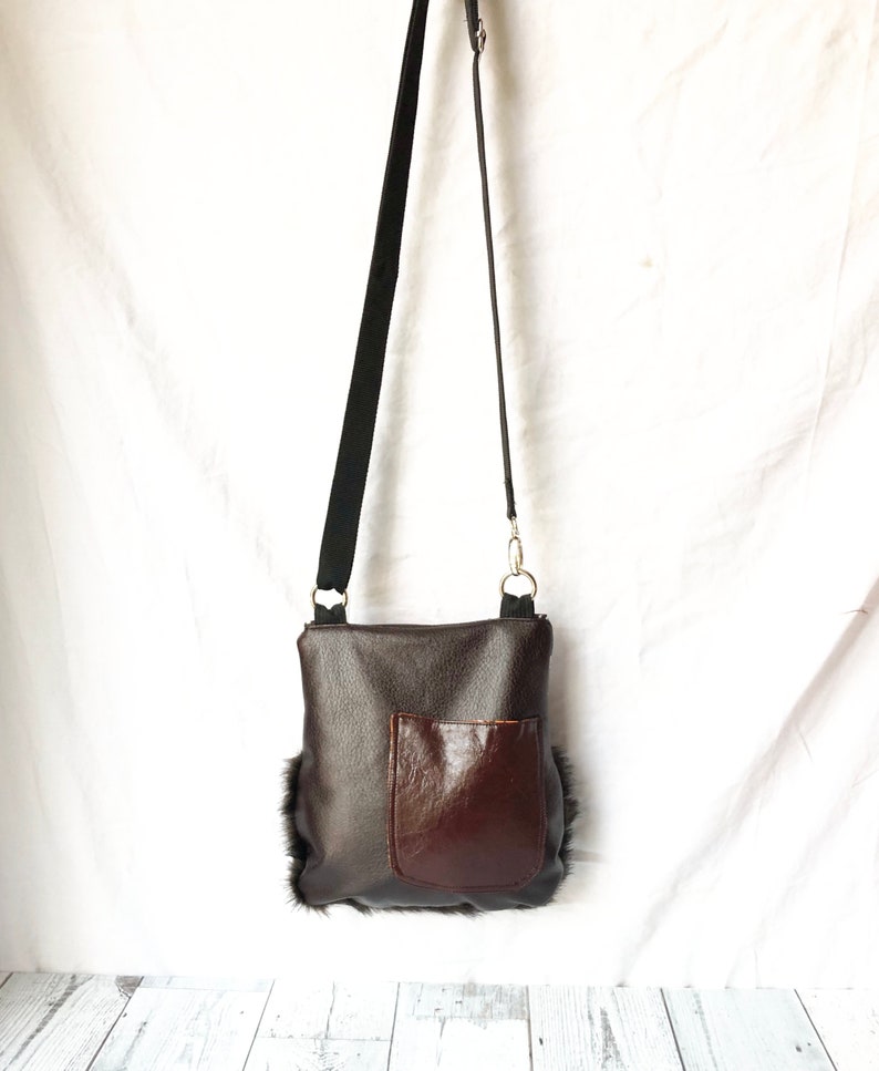 Pu&ograve; includere: Una borsa a tracolla in pelle marrone con una tasca in pelle marrone sul davanti. La borsa ha una tracolla nera e un bordo in pelliccia.