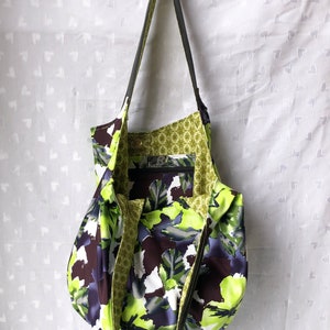 May include: A green and black floral print tote bag with a black shoulder strap and a green and gold patterned lining. The bag has a label that says "Kuchi" on it.