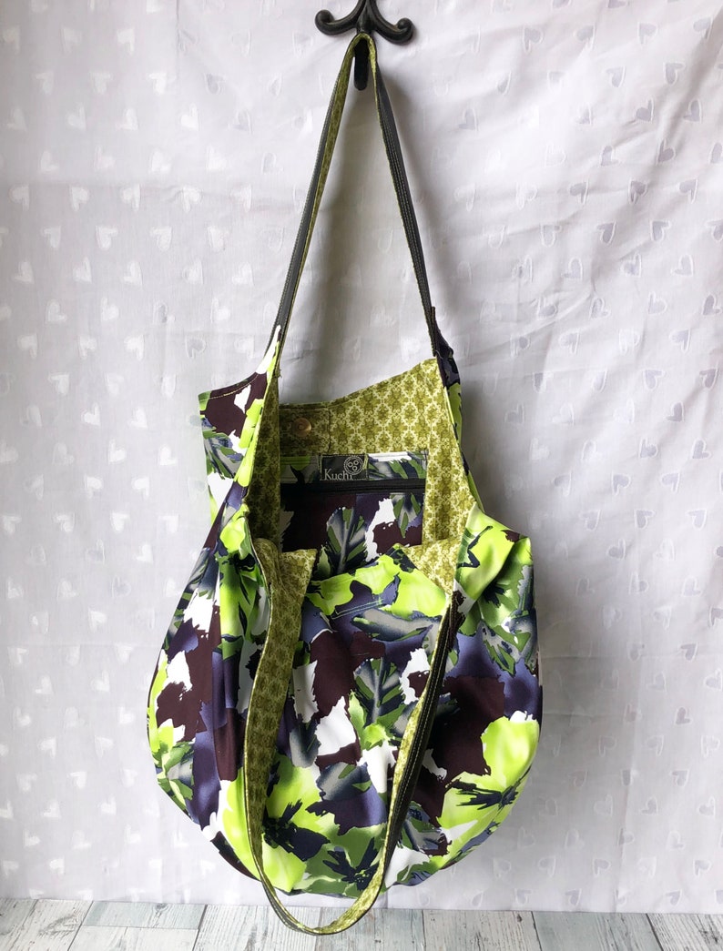 May include: A green and black floral print tote bag with a black shoulder strap and a green and gold patterned lining. The bag has a label that says "Kuchi" on it.