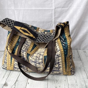 May include: A large tote bag with brown straps and a colorful patterned fabric design featuring blue, yellow, and white. The fabric has a geometric and abstract design.
