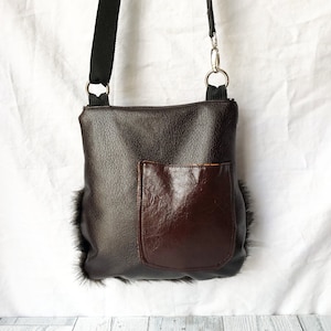Pu&ograve; includere: Una borsa a tracolla in pelle marrone con una tasca in pelle marrone sul davanti. La borsa ha una tracolla nera ed &egrave; rifinita con pelliccia nera.