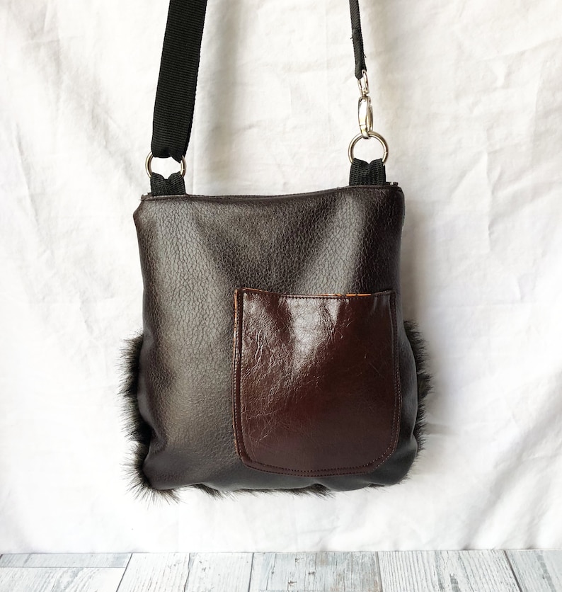 Pu&ograve; includere: Una borsa a tracolla in pelle marrone con una tasca in pelle marrone sul davanti. La borsa ha una tracolla nera ed &egrave; rifinita con pelliccia nera.