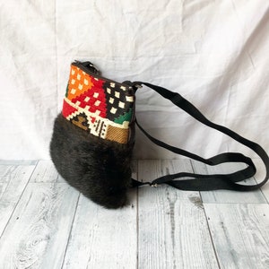 Pu&ograve; includere: Una borsa a tracolla nera e marrone con una patta a fantasia colorata e un bordo in pelliccia sintetica. La borsa ha una lunga tracolla regolabile.