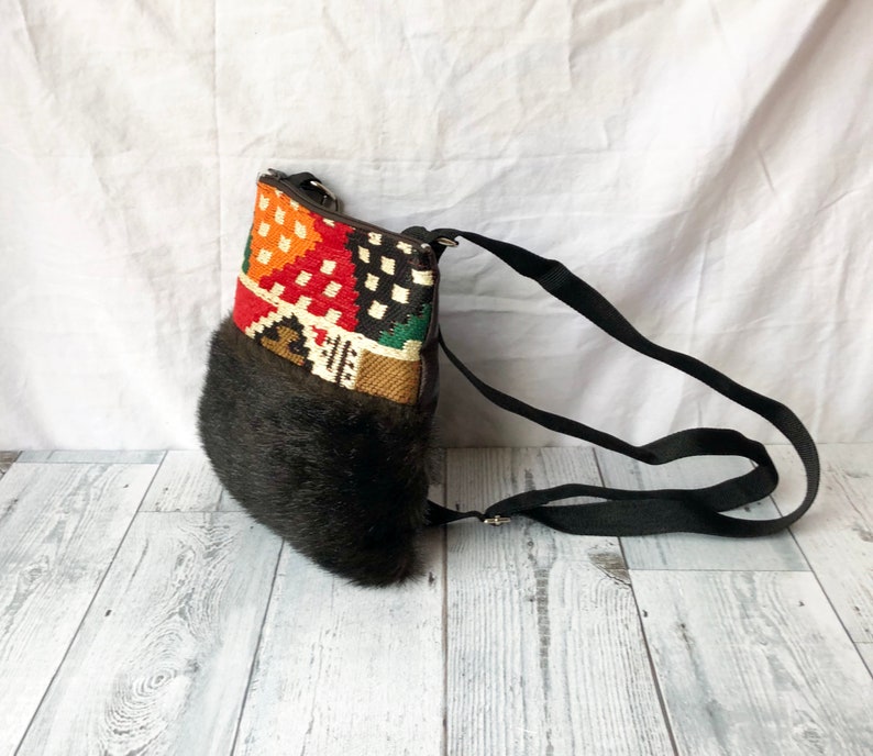 Pu&ograve; includere: Una borsa a tracolla nera e marrone con una patta a fantasia colorata e un bordo in pelliccia sintetica. La borsa ha una lunga tracolla regolabile.
