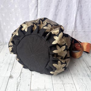 Op de afbeelding: Zwarte stoffen tas met gouden bloemenborduursel. De tas heeft een trekkoord sluiting en een lange band.