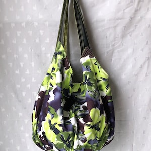 May include: A large, green, purple, and white floral print tote bag with two green and brown straps.