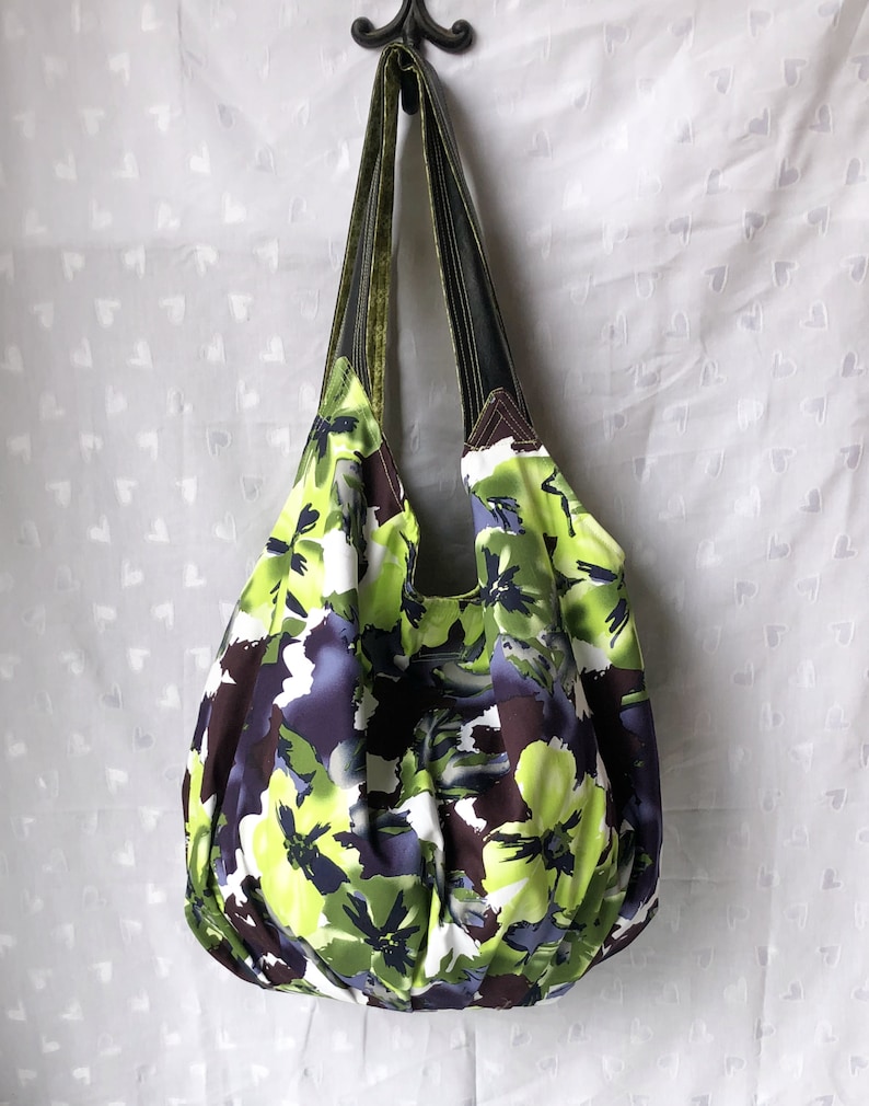 May include: A large, green, purple, and white floral print tote bag with two green and brown straps.