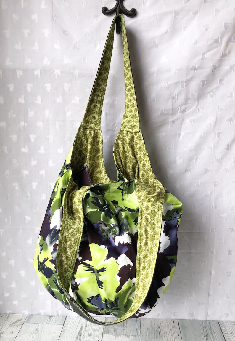 May include: A large green and white floral print tote bag with a green and gold patterned strap. The bag is hanging from a hook.