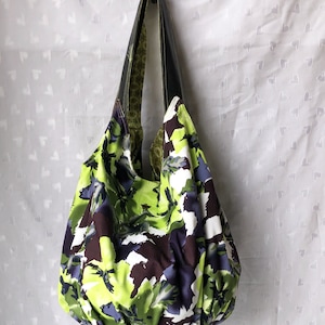May include: A large, green, white, and purple floral print tote bag with black leather handles.