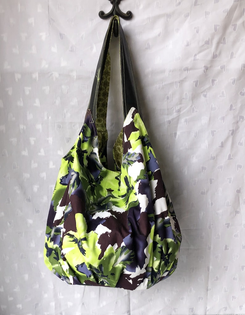May include: A large, green, white, and purple floral print tote bag with black leather handles.