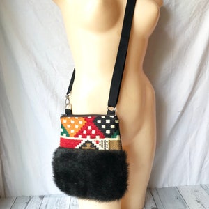 Pu&ograve; includere: Una piccola borsa a tracolla con un motivo geometrico colorato e un bordo in pelliccia sintetica nera. La borsa ha una tracolla nera regolabile.