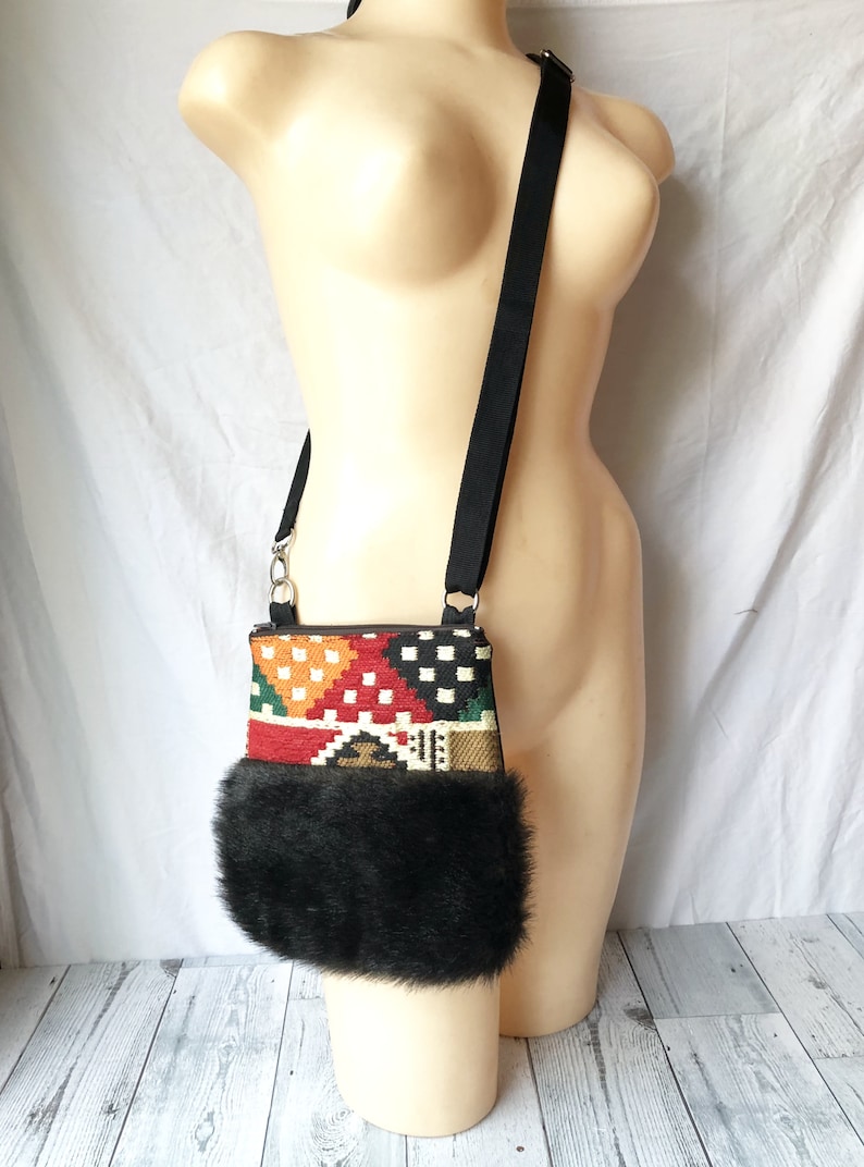 Pu&ograve; includere: Una piccola borsa a tracolla con un motivo geometrico colorato e un bordo in pelliccia sintetica nera. La borsa ha una tracolla nera regolabile.