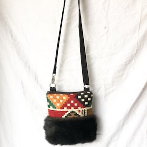 Pu&ograve; includere: Una piccola borsa a tracolla colorata con motivo geometrico e bordatura in pelliccia nera. La borsa ha una tracolla nera regolabile e una cerniera argentata.