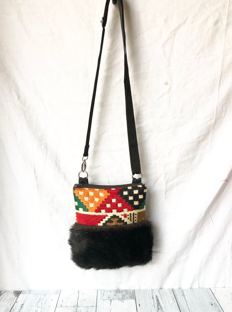 Pu&ograve; includere: Una piccola borsa a tracolla colorata con motivo geometrico e bordatura in pelliccia nera. La borsa ha una tracolla nera regolabile e una cerniera argentata.
