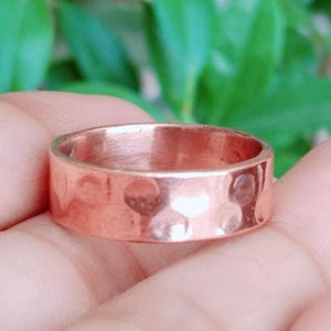 Peut inclure: Une bague en cuivre présentant une surface martelée et texturée avec une finition polie. L'anneau a une largeur constante et un profil arrondi, mettant en valeur la couleur brun rougeâtre métallique et les indentations du martelage.