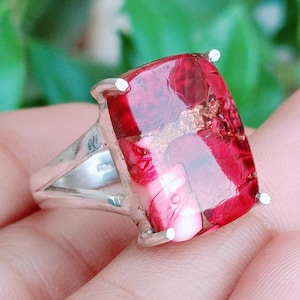 May include: A silver ring featuring a large, rectangular, polished red gemstone with visible dark red and white marbling patterns. The stone is held in place by four silver prongs on a simple, smooth, polished silver band that tapers toward the back.