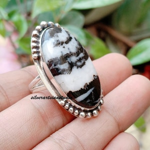May include: A sterling silver ring featuring a large, oval-shaped white and black patterned stone set in a bezel. The setting is decorated with a beaded border along the edge. The band is made of polished silver and the text silverartsianstudio is visible.