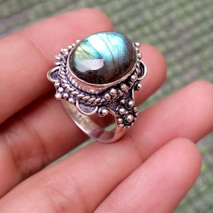 May include: A sterling silver ring featuring a large, oval-shaped labradorite gemstone with blue and green iridescence. The setting is decorated with intricate twisted rope patterns and small silver beads surrounding the central stone.