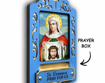 May include: A blue wooden wall plaque featuring a central image of Saint Veronica holding a cloth with the face of Jesus. The frame has gold scrollwork, a cross at the top, and a gold plate with the text St. Veronica PRAY FOR US.