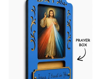 May include: A blue wooden prayer box featuring a central image of Jesus with red and blue rays. The top has a cutout cross and scrollwork. A rectangular plaque at the bottom displays the text, Jesus, I trust in You, in black script.