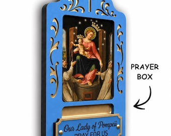 May include: A blue wooden prayer box featuring a central religious image of Our Lady of Pompeii with the infant Jesus. The frame has gold-toned scrollwork, a cross at the top, and a plaque at the bottom with the text Our Lady of Pompeii PRAY FOR US.