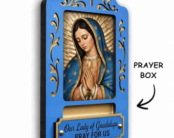 May include: A blue wall-mounted prayer box featuring a central image of Our Lady of Guadalupe with a gold halo. The frame has decorative cutouts and a cross at the top. A gold plaque at the bottom reads, Our Lady of Guadalupe PRAY FOR US.
