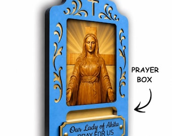 May include: A blue wooden wall-mounted prayer box featuring a central carved wooden figure of Our Lady of Akita against a sunburst background. The frame has decorative cutouts, a cross at the top, and a plaque reading Our Lady of Akita PRAY FOR US.