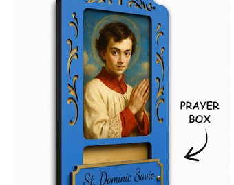 May include: A blue wall-mounted prayer box featuring a portrait of St. Dominic Savio with hands clasped in prayer. The frame has a cutout cross at the top and a gold-toned plaque at the bottom with the text St. Dominic Savio PRAY FOR US.