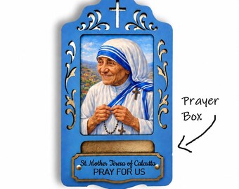 May include: A blue wooden wall-mounted prayer box featuring a cutout cross at the top and an image of Mother Teresa holding a rosary. Below the image is a small compartment and a plaque with the text St. Mother Teresa of Calcutta PRAY FOR US.