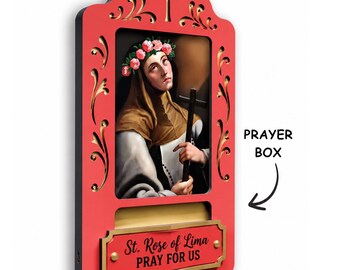 May include: A red wooden prayer box featuring a central image of St. Rose of Lima wearing a floral crown and holding a cross. The frame has gold scrollwork and a cross at the top. A plaque at the bottom reads St. Rose of Lima PRAY FOR US.