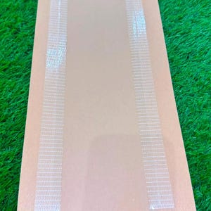 May include: A rectangular tan paper sleeve featuring a vertical transparent plastic window running down the center. The sleeve has two parallel strips of white adhesive tape applied along the edges of the clear plastic section for secure closure.