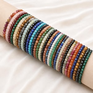 Könnte beinhalten: Eine Sammlung zahlreicher elastischer Armbänder aus kleinen, facettierten, mehrfarbigen Edelsteinperlen. Die Armbänder weisen eine große Vielfalt an Farben auf, darunter Rot-, Rosa-, Grün-, Braun-, Schwarz-, Blau-, Türkis- und Weißtöne.