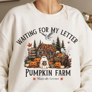 May include: A cream-colored crewneck sweatshirt featuring a graphic print with the text "WAITING FOR MY LETTER PUMPKIN FARM Magically Grown". The design includes a ghost, pumpkins, a wooden house, a wagon, an owl, and a flying unicorn.