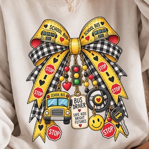 Puede incluir: Una sudadera blanca de cuello redondo con un gran gráfico de un lazo amarillo y negro a cuadros. El lazo está decorado con iconos de autobuses escolares, señales de stop, un semáforo, un volante, una cara sonriente y una etiqueta que dice BUS DRIVER SAFE KIDS BRIGHT FUTURES.