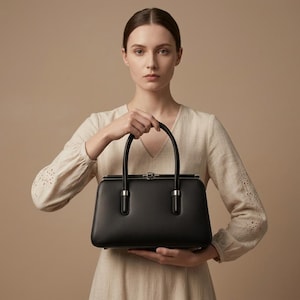 May include: A structured black handbag with a smooth finish, featuring two rounded top handles, a silver-toned metal frame, and a secure clasp closure. The bag has a rectangular base and clean, minimalist lines, showcasing a polished appearance.