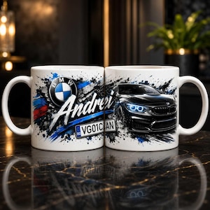 Può includere: Una tazza in ceramica bianca con la grafica di un'auto BMW nera, il logo BMW, schizzi di vernice blu e nera, il nome Andrei in corsivo bianco e una targa con il testo VG01CAN, posizionata su una superficie scura e riflettente.